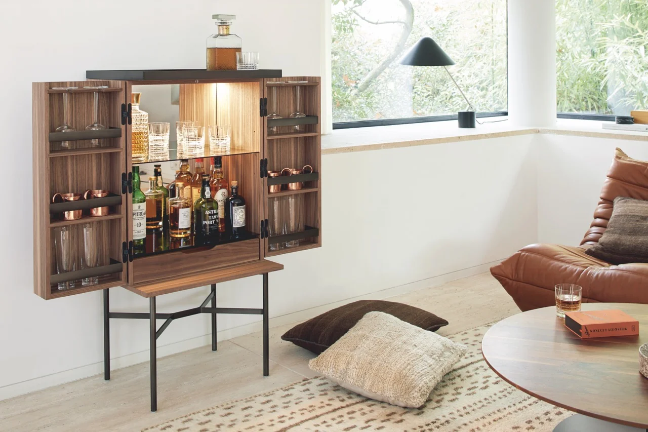 Barschrank HARRI von Peter Fehrentz in Holzoptik mit schwarzem Rahmen, geöffnet in modernem Wohnzimmer mit Tageslicht und Pflanzen im Hintergrund.