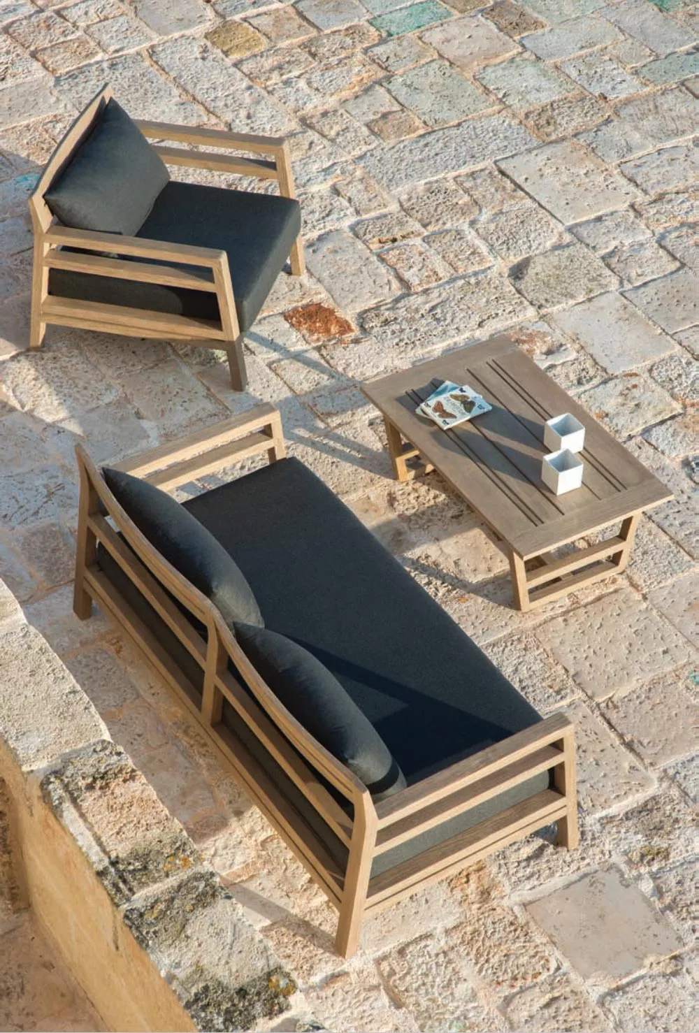 Ethimo Costes Loungegruppe in Naturholz mit schwarzen Kissen auf einer Steinplatte von oben fotografiert.