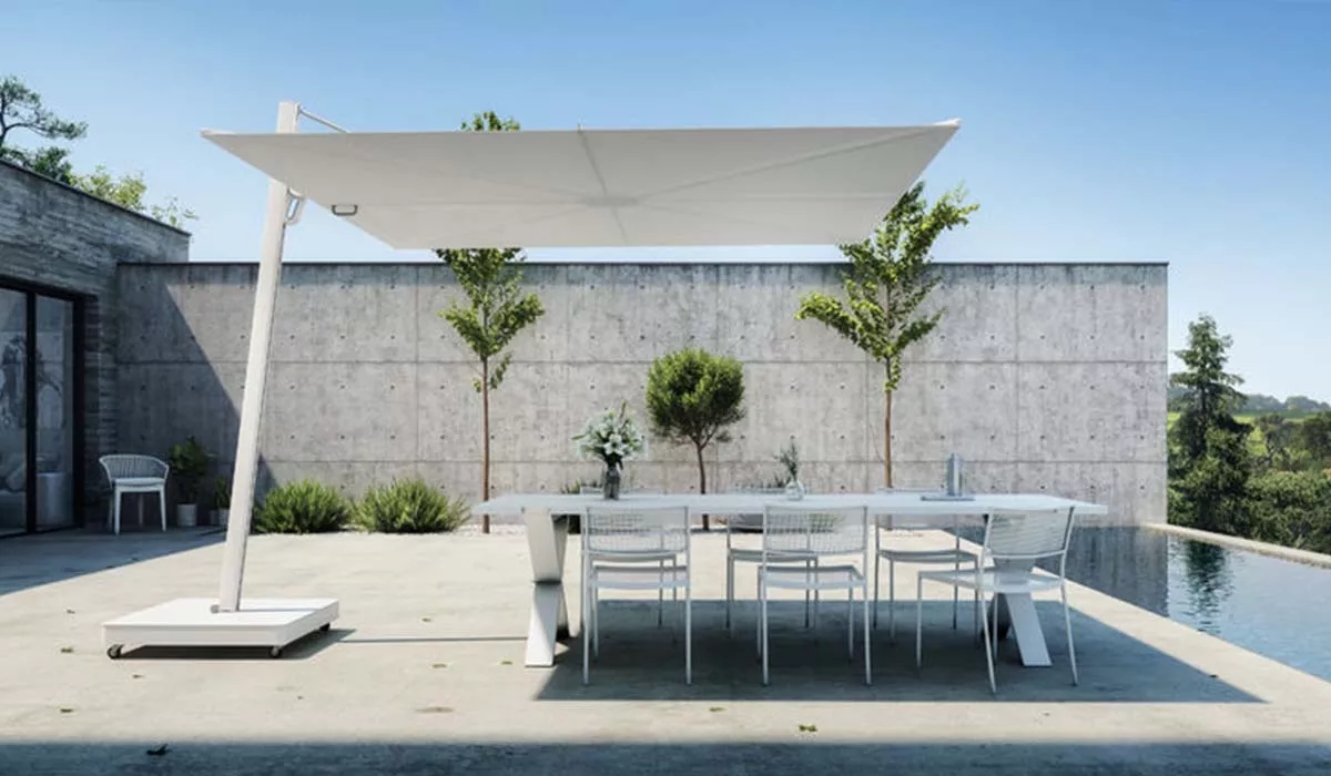 Weiße Spactraux-Kollektion Sonnenschirm auf modernem Beton-Terrassenbereich mit Tisch und Stühlen, umgeben von minimalistischer Gartenlandschaft.