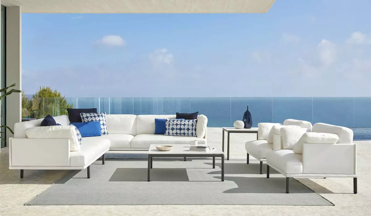 POINT Long Island Outdoor-Loungegruppe in Weiß auf Terrasse mit Meerblick, bestehend aus Sofas, Tisch und blauen Kissen, stimmungsvolles Ambiente.