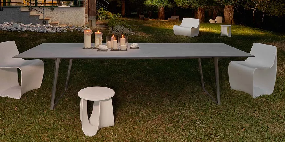MDF Italia Sag Tisch in Grau, umgeben von weißen Stühlen, auf einer Wiese bei Dämmerung, mit Kerzen als stimmungsvolle Dekoration.