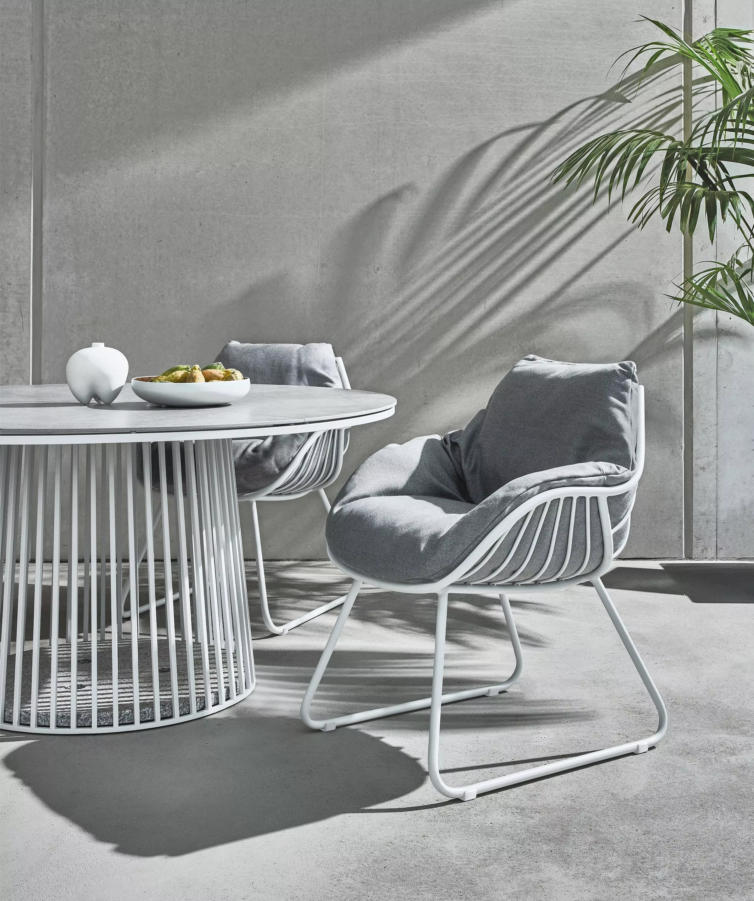Zwei Solpuri Chill Sessel und ein runder Tisch mit Obstschale in einem modernen Außenbereich mit Betonwand und Pflanze im Hintergrund