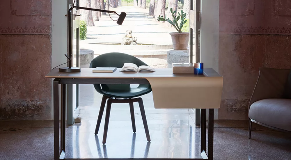 Poltrona Frau Fred Stuhl in Dunkelgrün vor einem Schreibtisch in einem eleganten Raum mit Blick auf einen sonnigen Garten.