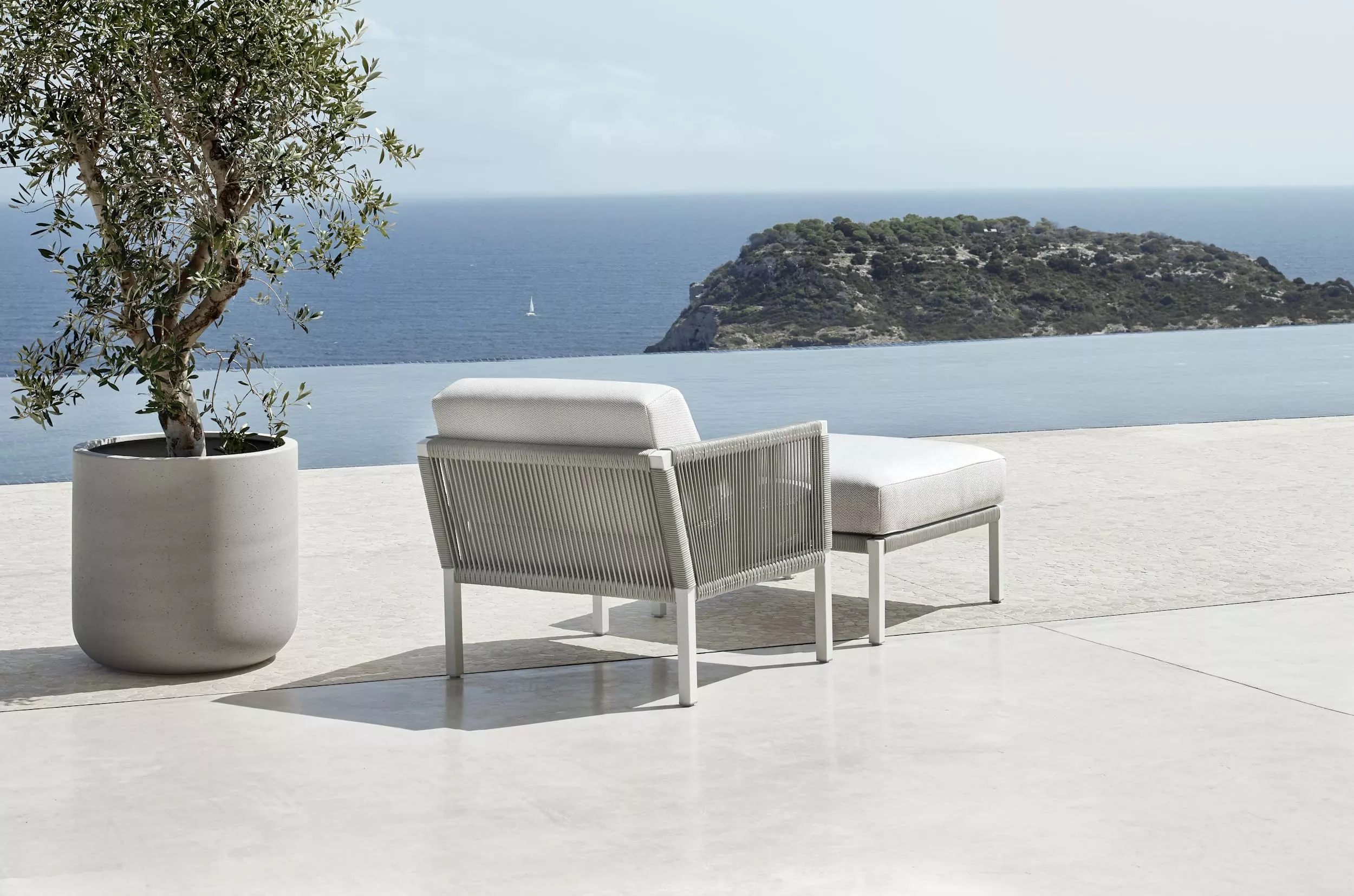 Solpuri Club A Lounge Sessel und Hocker in einer modernen Außenumgebung mit Meerblick und einem Olivenbaum im Hintergrund