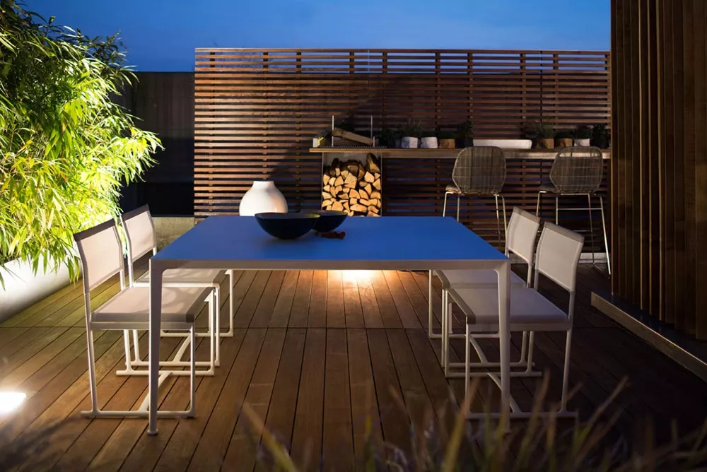 B&B Italia Mirto Outdoor Esstisch auf einer stilvollen Terrasse bei Nacht mit modernen weißen Stühlen und Pflanzen im Hintergrund