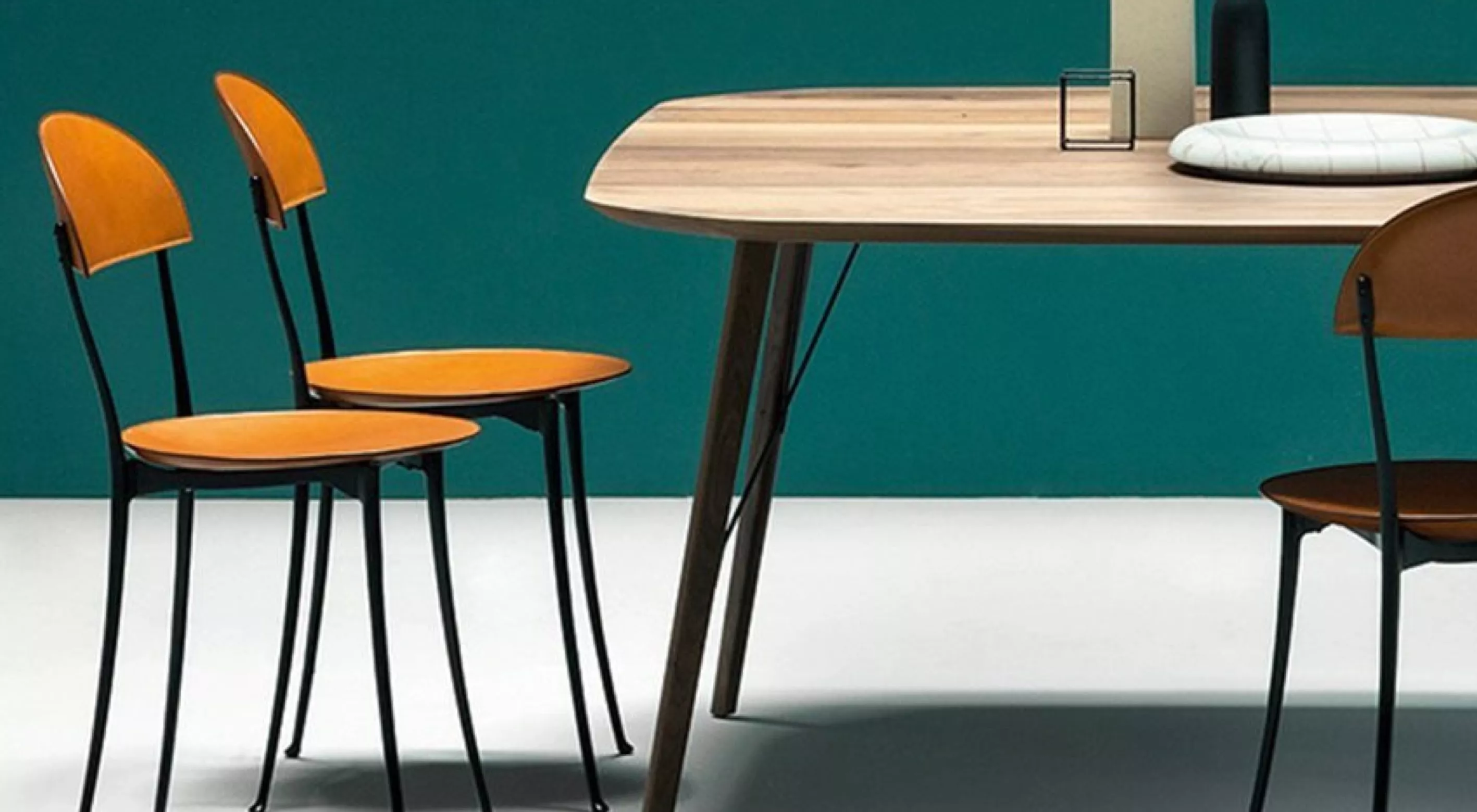 Zwei orange Zanotta Tonietta Stühle stehen neben einem Holztisch in einem modernen Esszimmer mit grüner Wand im Hintergrund.