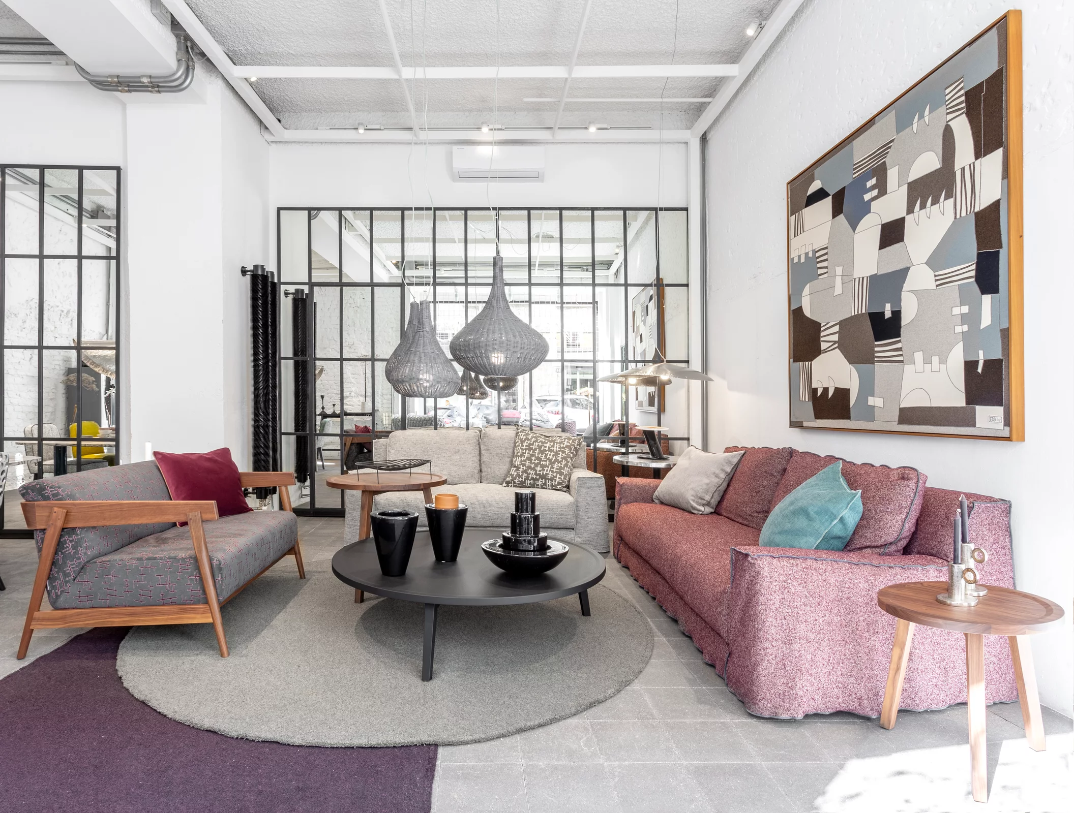 Ein Wohnzimmer mit modernen Möbeln von Gervasoni darunter ein rotes Sofa ein grauer Sessel ein runder Couchtisch und dekorative Lampen im Hintergrund.