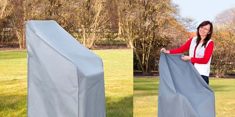 Frau zeigt graue Sesselhaube von Villa Schmidt im Garten, passend für große Sessel, mit Bäumen im Hintergrund.