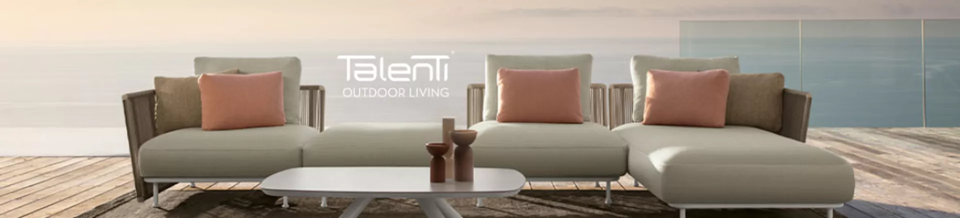 Talenti Outdoor Living Lounge-Set in Beige mit rosa Kissen auf Holzterrasse vor Meereshintergrund.