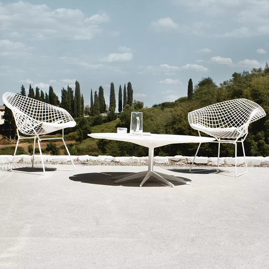 Zwei Knoll Harry Bertoia Diamond Chairs und ein Tisch stehen auf einer Terrasse mit Blick auf eine Landschaft mit Bäumen und blauem Himmel.