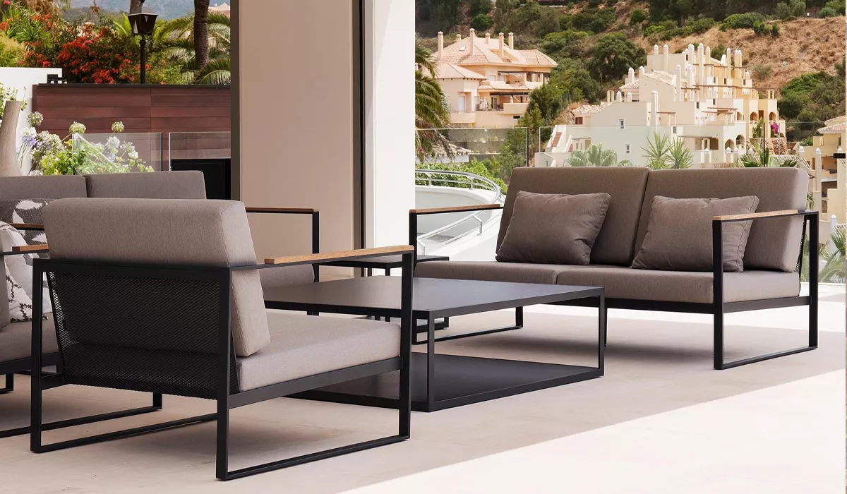 Roshults Loungemöbel in Grau auf einer Terrasse mit Blick auf eine mediterrane Landschaft, bestehend aus Sofa, Sessel und Tisch.