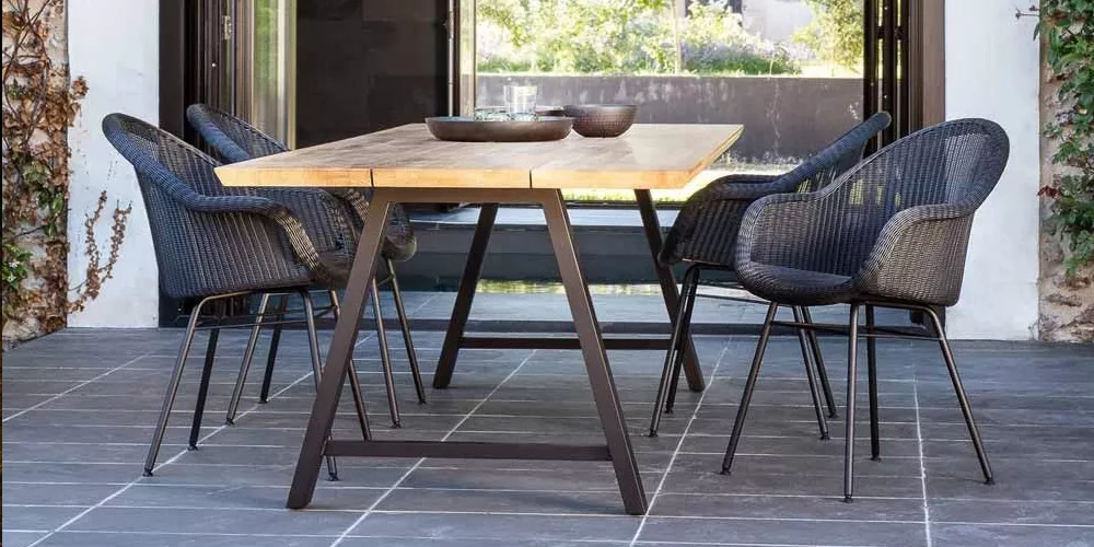 Vincent Sheppard Edgard Esstisch-Set mit schwarzem Metallgestell und Holzplatte auf einer Terrasse mit Gartenblick.