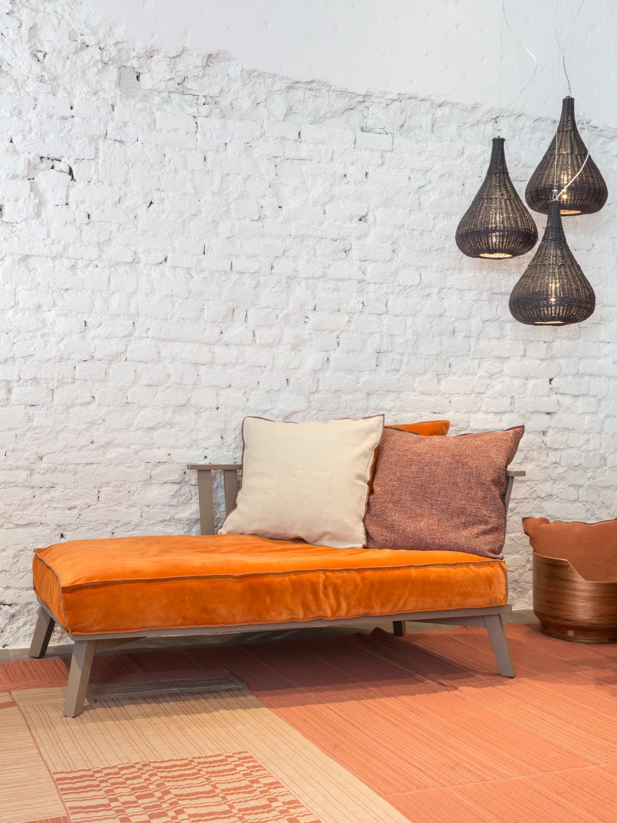 Gervasoni Sofa mit orangefarbenem Bezug und Kissen in einem gemütlichen Raum mit weißen Backsteinwänden und hängenden Lampen