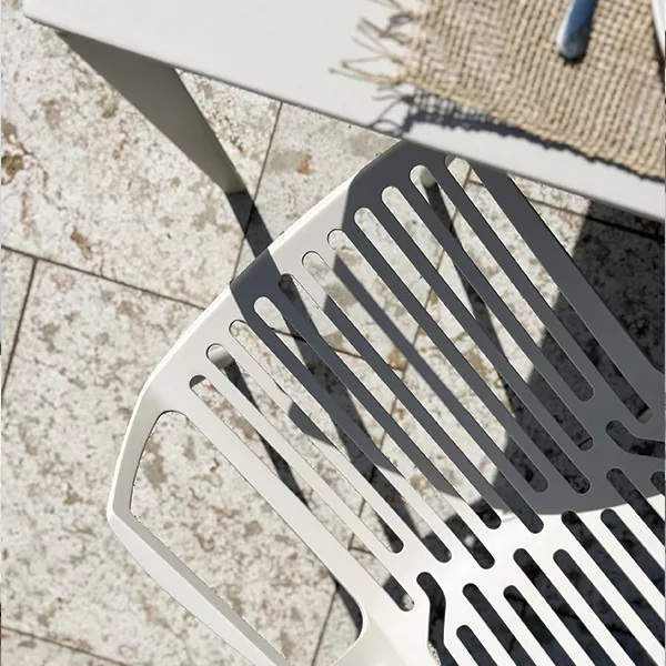 Heller Gartenstuhl aus Metall neben einem Tisch auf einer Steinfliese, fotografiert aus der Vogelperspektive bei Sonnenschein.