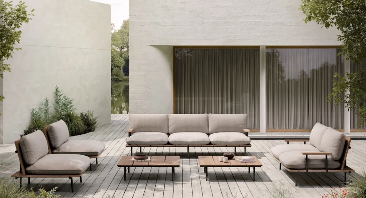 Bivaq Nami Outdoor-Möbelset in Beige auf einer Holzterrasse vor einem modernen Gebäude mit großen Fenstern und grüner Umgebung.