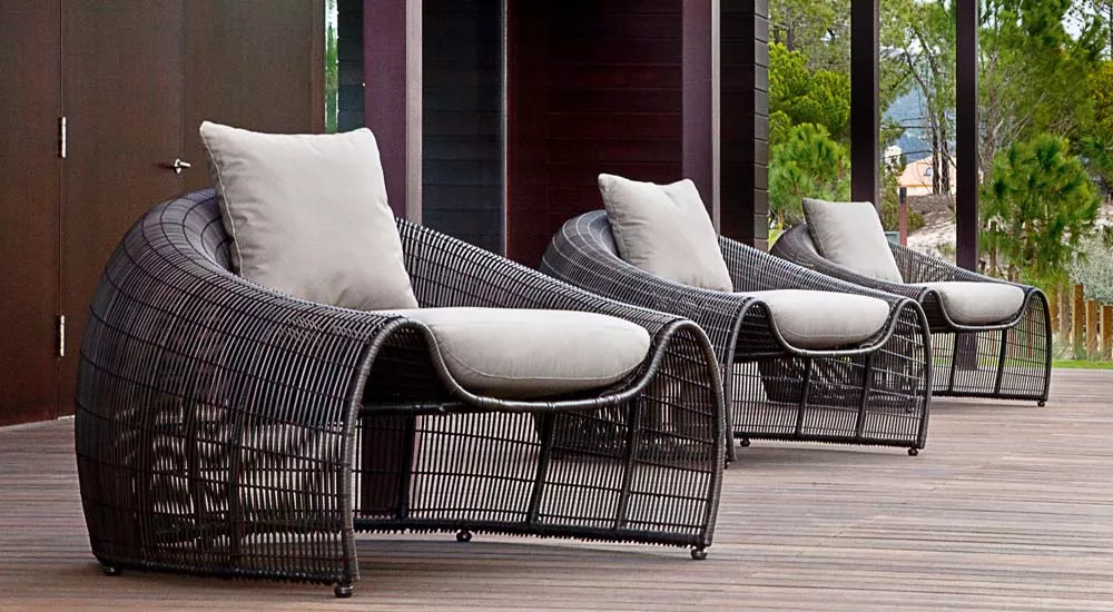 Zwei Kenneth Cobonpue Croissant Kaffeetische in Schwarz auf einer Holzterrasse mit grüner Waldkulisse im Hintergrund.