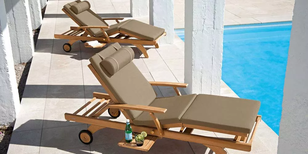 Barlow Tyrie Capri Sonnenliege in Beige auf einer Terrasse am Pool, aus Teakholz mit verstellbarer Rückenlehne und Rädern für einfache Bewegung.