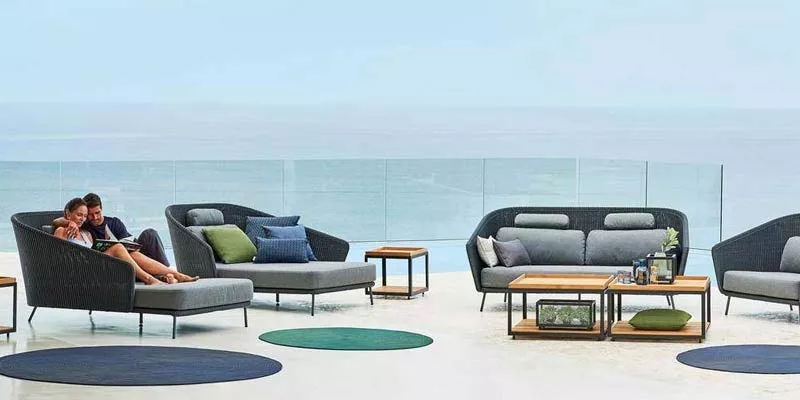 Cane-line Mega Loungegruppe in Anthrazit auf einer Terrasse mit Meerblick, bestehend aus Sofas, Sesseln und Tischen, in entspannter Atmosphäre.