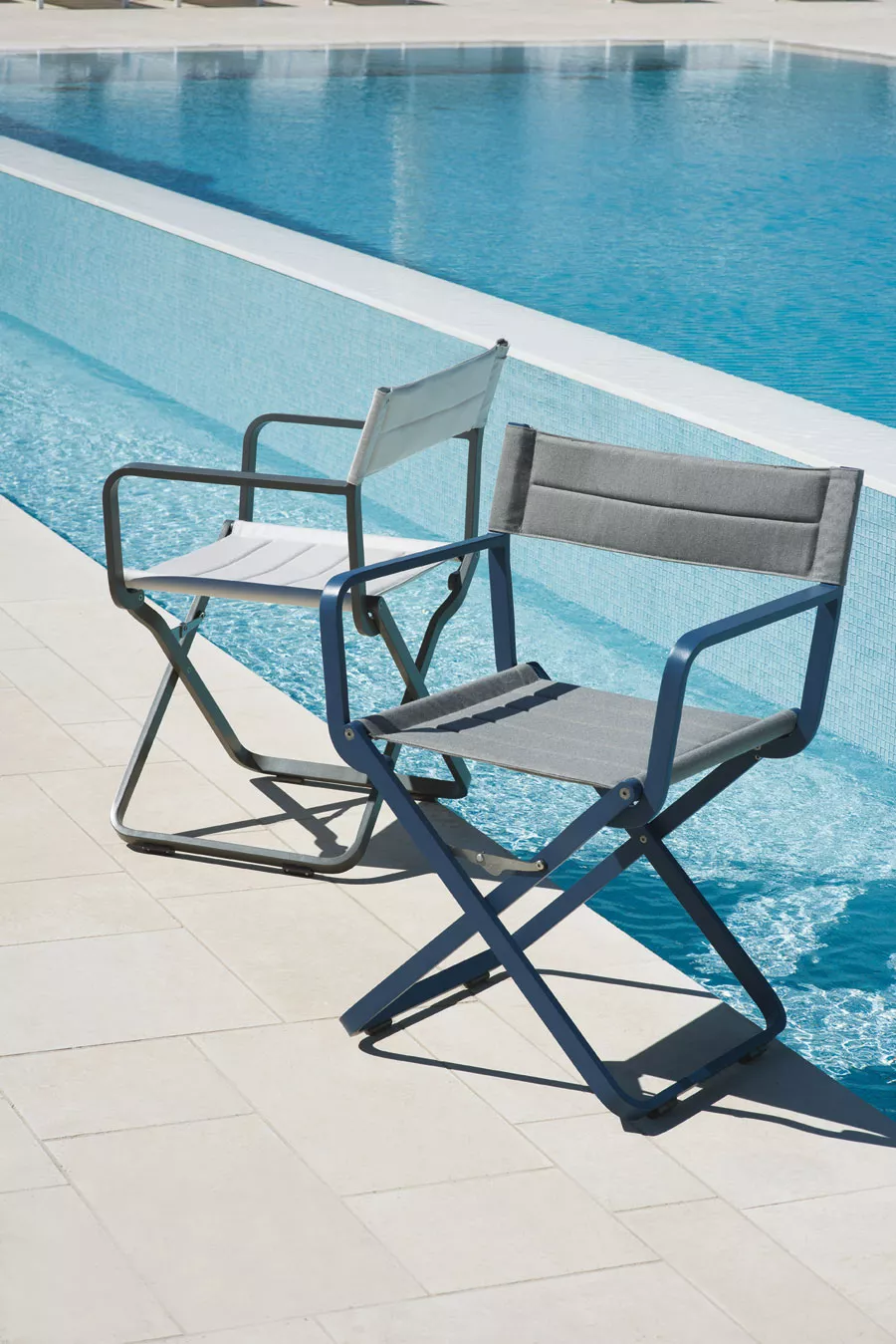 Zwei klappbare Ethimo Studios Armlehnstühle in Grau und Weiß stehen auf einer Terrasse am Pool.
