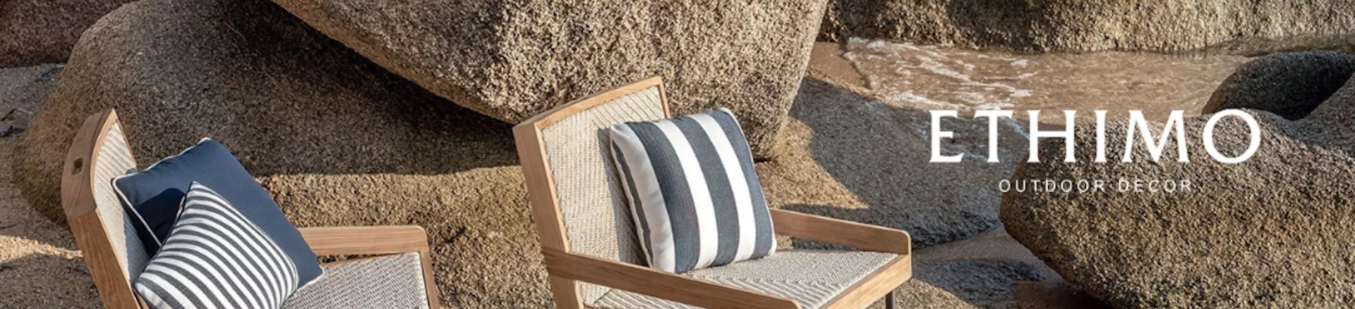 Zwei Ethimo Outdoor-Dekor-Stühle aus hellem Holz mit gestreiften Kissen vor einer felsigen Strandkulisse.