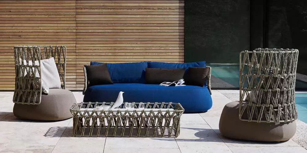 B&B Italia Fat Outdoor Loungegruppe mit Loungesofa und Sesseln auf einer Terrasse vor einer Holzwand und einem Pool im Hintergrund