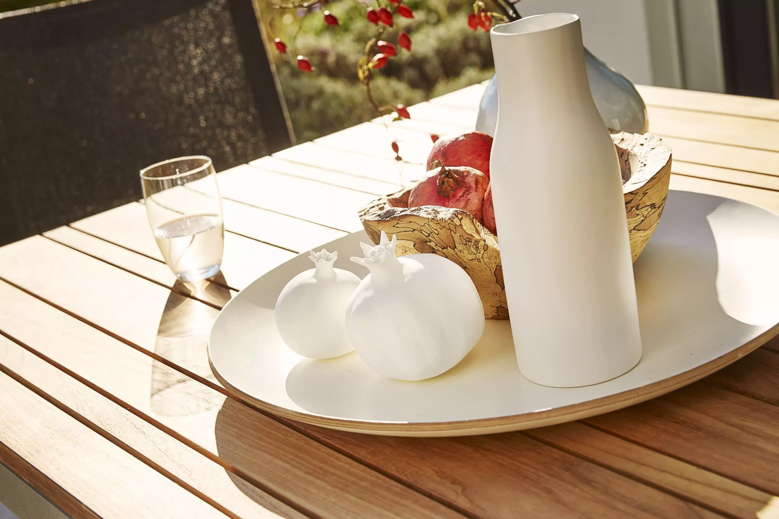 Solpuri Classic Tisch Alu auf einer Terrasse mit einer Vase zwei Dekorationsobjekten einem Glas Wasser und einem Obstkorb im Sonnenlicht