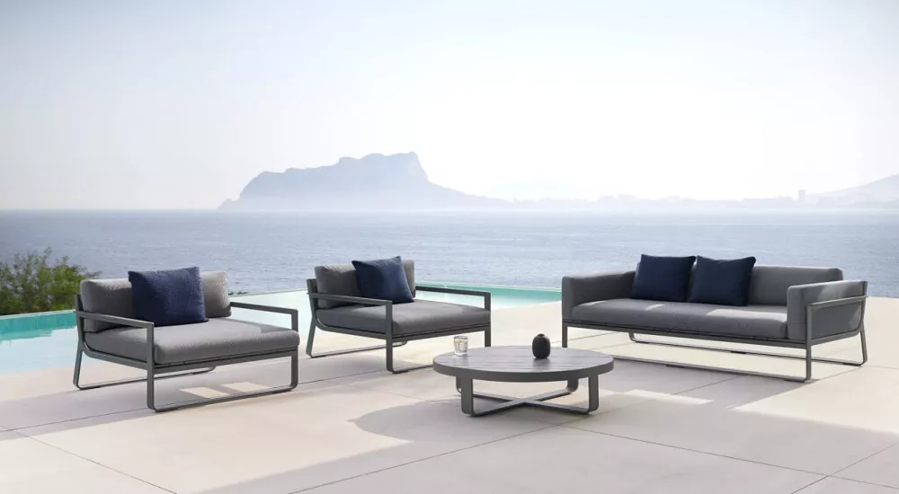 Anthrazitfarbene Flat Lounge-Möbel von Villa Schmidt mit 2-Sitzer-Sofa, Sessel und rundem Couchtisch vor Meereshintergrund.