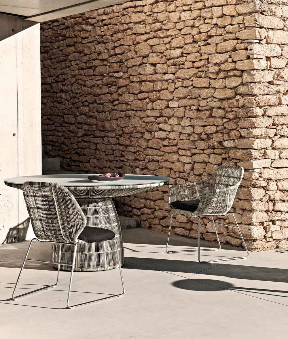B&B Italia Crinoline Outdoor Essgruppe bestehend aus einem runden Tisch und zwei Stühlen in einem modernen Außenbereich vor einer Steinmauer