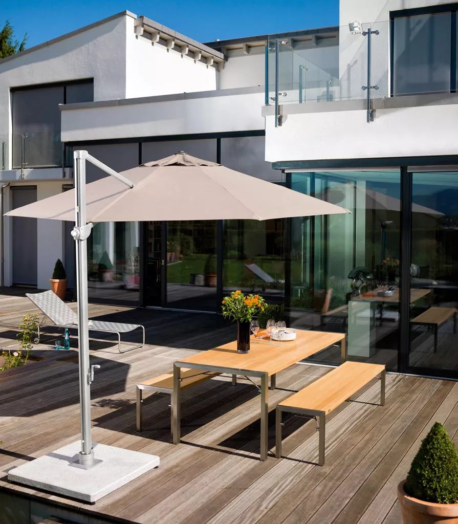 Freiarm-Sonnenschirm von Weishäupl in Beige auf einer modernen Holzterrasse vor einem weißen Haus, stimmungsvolle Sommeratmosphäre.
