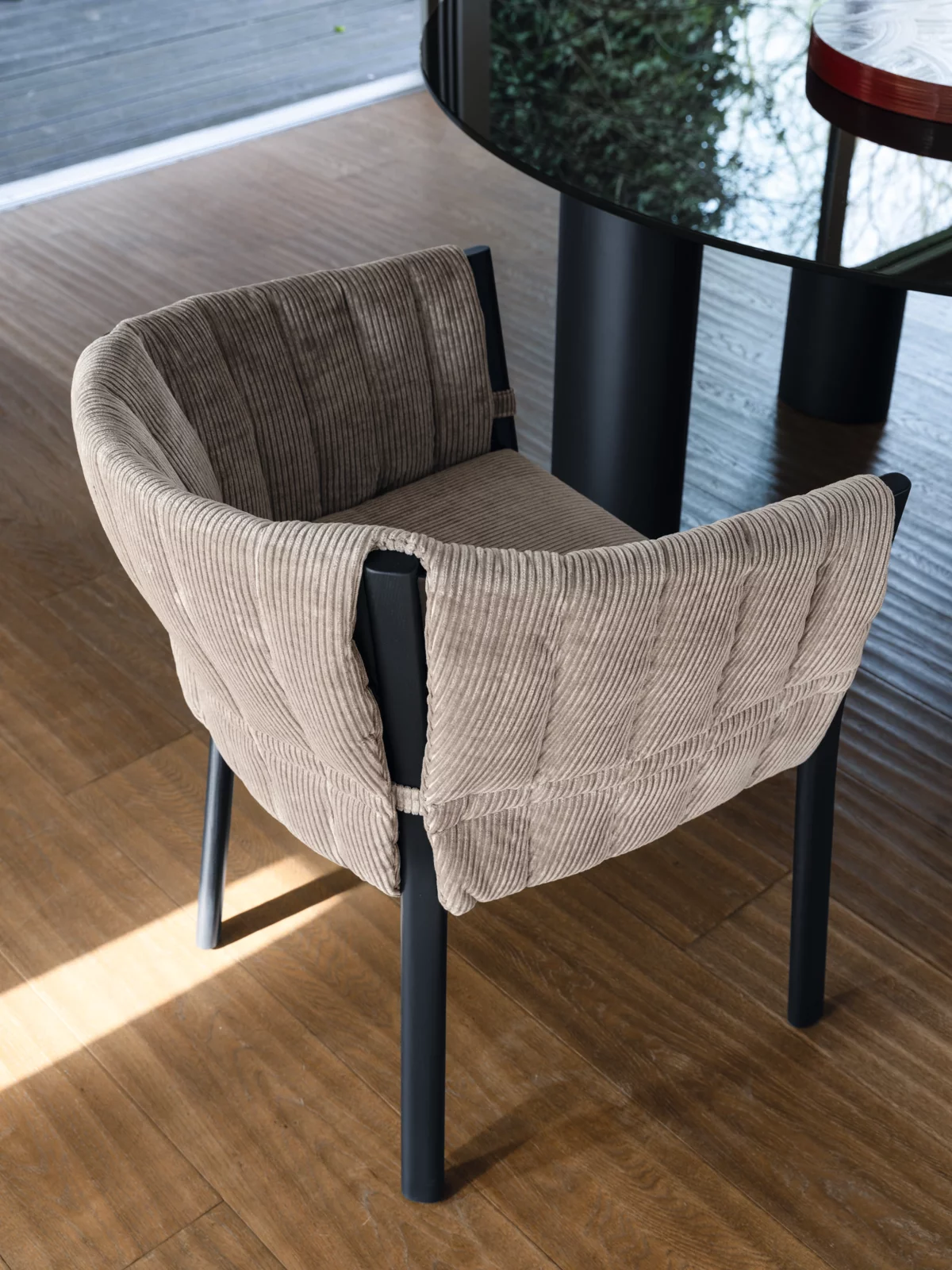 Gervasoni Brick 23 Stuhl mit beigem Stoffbezug und schwarzen Beinen steht auf einem Holzboden neben einem schwarzen Tisch