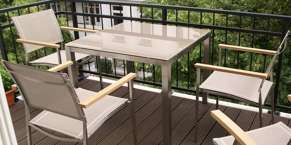 Royal Mirage Casino Gartenmöbel-Set in Beige auf einem Balkon mit Blick auf grüne Bäume, bestehend aus Tisch und vier Stühlen.