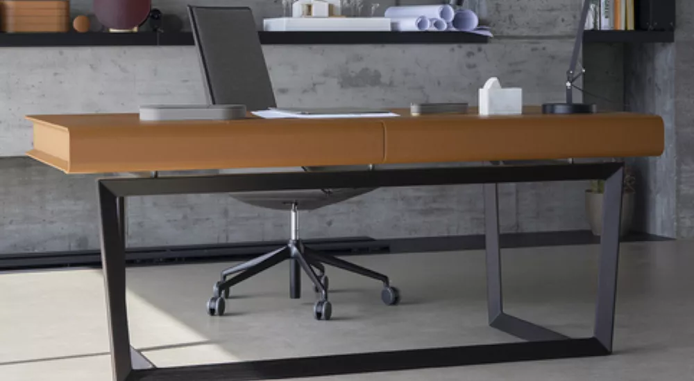 Poltrona Frau Peek-A-Book Schreibtisch in Cognacbraun, modernes Design, in einem minimalistischen Büro mit Betonwand und grauem Boden.