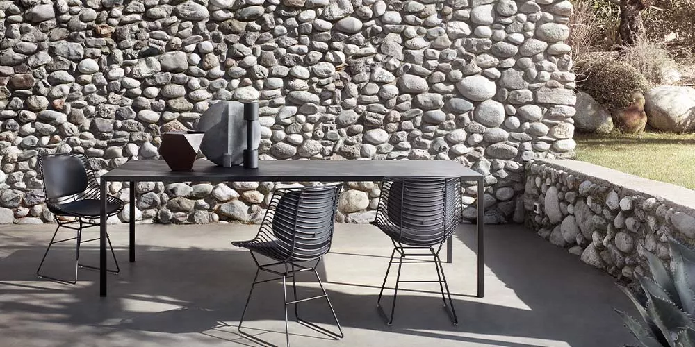 MDF Italia Flow Filo Stühle in Schwarz um einen modernen Tisch auf einer Terrasse mit Steinmauer im Hintergrund.