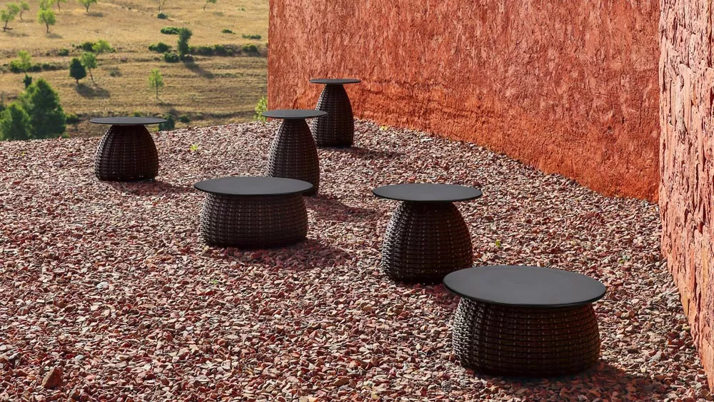 Dedon Porcini Beistelltische stehen auf einem Kiesboden neben einer roten Wand in einer ländlichen Umgebung.