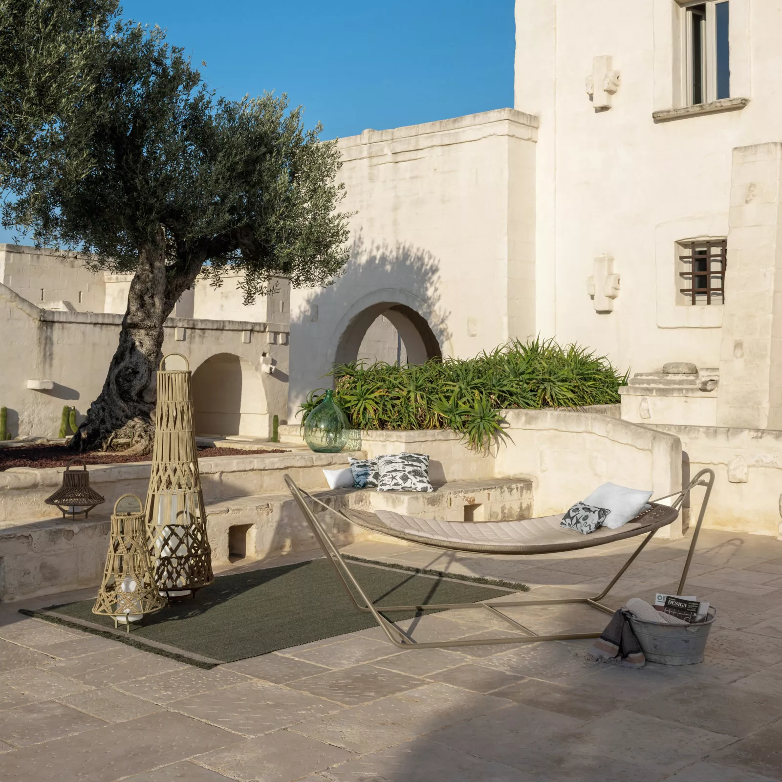 Talenti Panama Hängematte mit Gestell in Beige auf einer sonnigen Terrasse vor einer historischen Steinmauer.