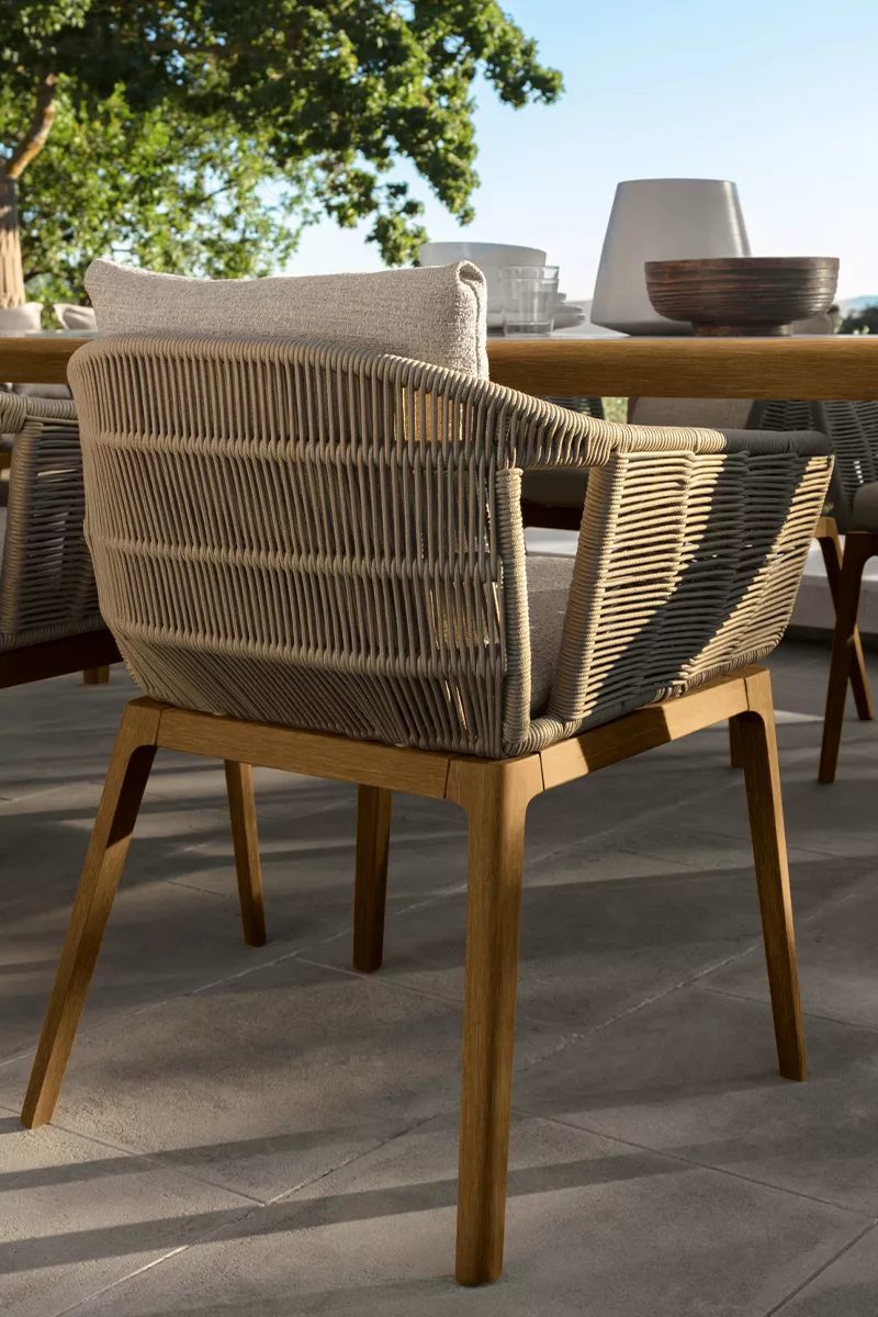 Talenti Cruise Teak Outdoor-Stuhl in natürlichem Teakholz und geflochtenem Seil, auf einer Terrasse mit Holztisch und Geschirr im Hintergrund.