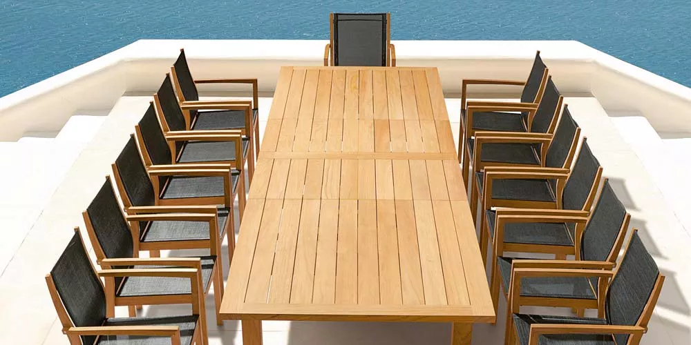 Barlow Tyrie Apex Essgruppe aus Teakholz mit schwarzen Textilene-Stühlen auf einer Terrasse mit Meerblick.