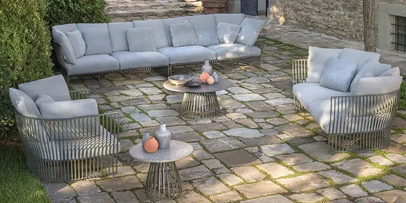 Ethimo Venexia Outdoor Loungegruppe in Grau auf einer gepflasterten Terrasse mit Steinmauer im Hintergrund, stimmungsvolle Gartenatmosphäre.