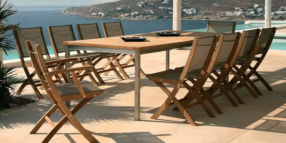 Barlow Tyrie Horizon Essgruppe aus Teakholz und Edelstahl auf einer Terrasse mit Meerblick, bestehend aus einem Tisch und acht Stühlen.