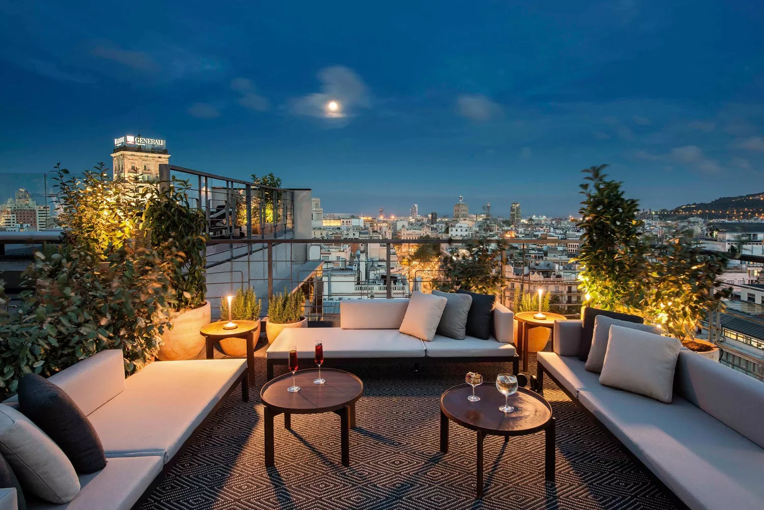 Bivaq NAK XL Loungegruppe in Grau auf einer Dachterrasse bei Nacht mit Blick auf die beleuchtete Stadt und den Vollmond im Hintergrund.