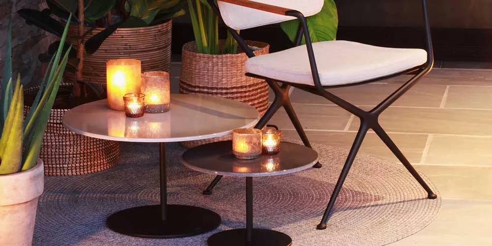 Royal Botania Butler Beistelltische in Schwarz und Beige, stimmungsvolle Abendaufnahme auf einer Terrasse mit Kerzenlicht.