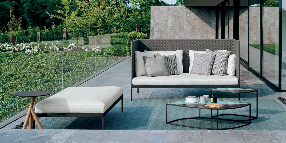 Roda Kollektion Basket, graues Sofa und weißer Hocker auf moderner Terrasse mit Glasgeländer und Garten im Hintergrund.