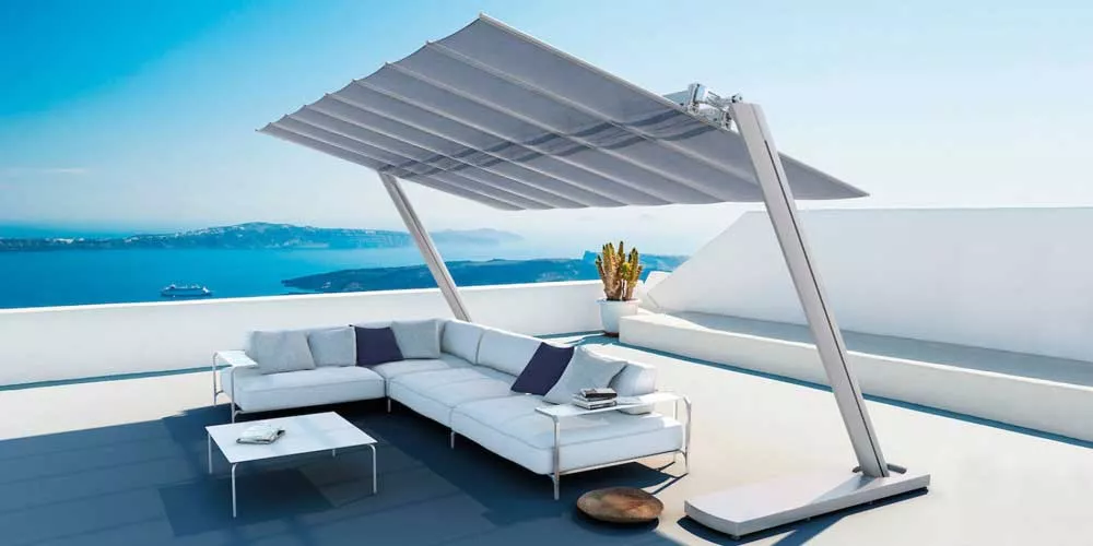 Ein FIM Flexy Zen Sonnenschirm in Grau auf einer modernen Dachterrasse mit Meerblick, neben einer weißen Lounge-Sitzgruppe.