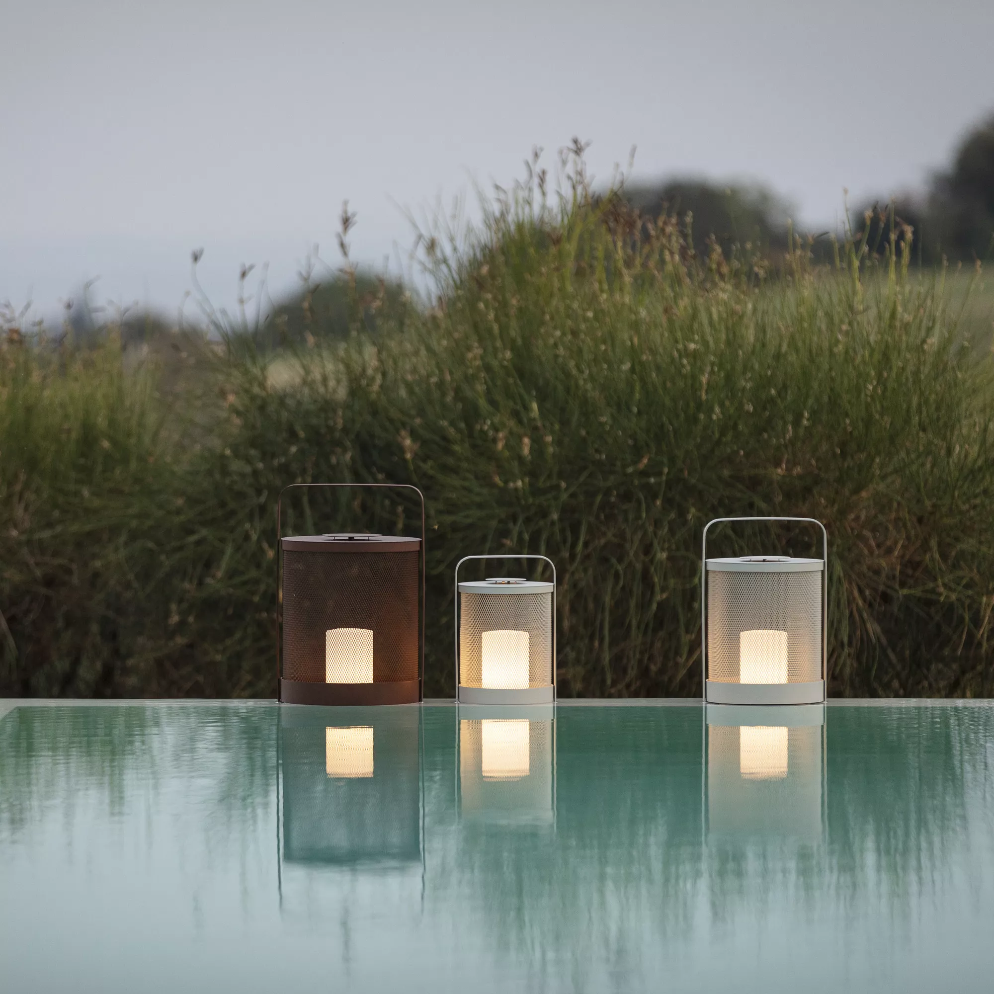 Drei Todus Outdoor-Leuchten in Braun und Weiß auf einem Tisch vor einer natürlichen Kulisse bei Dämmerung.