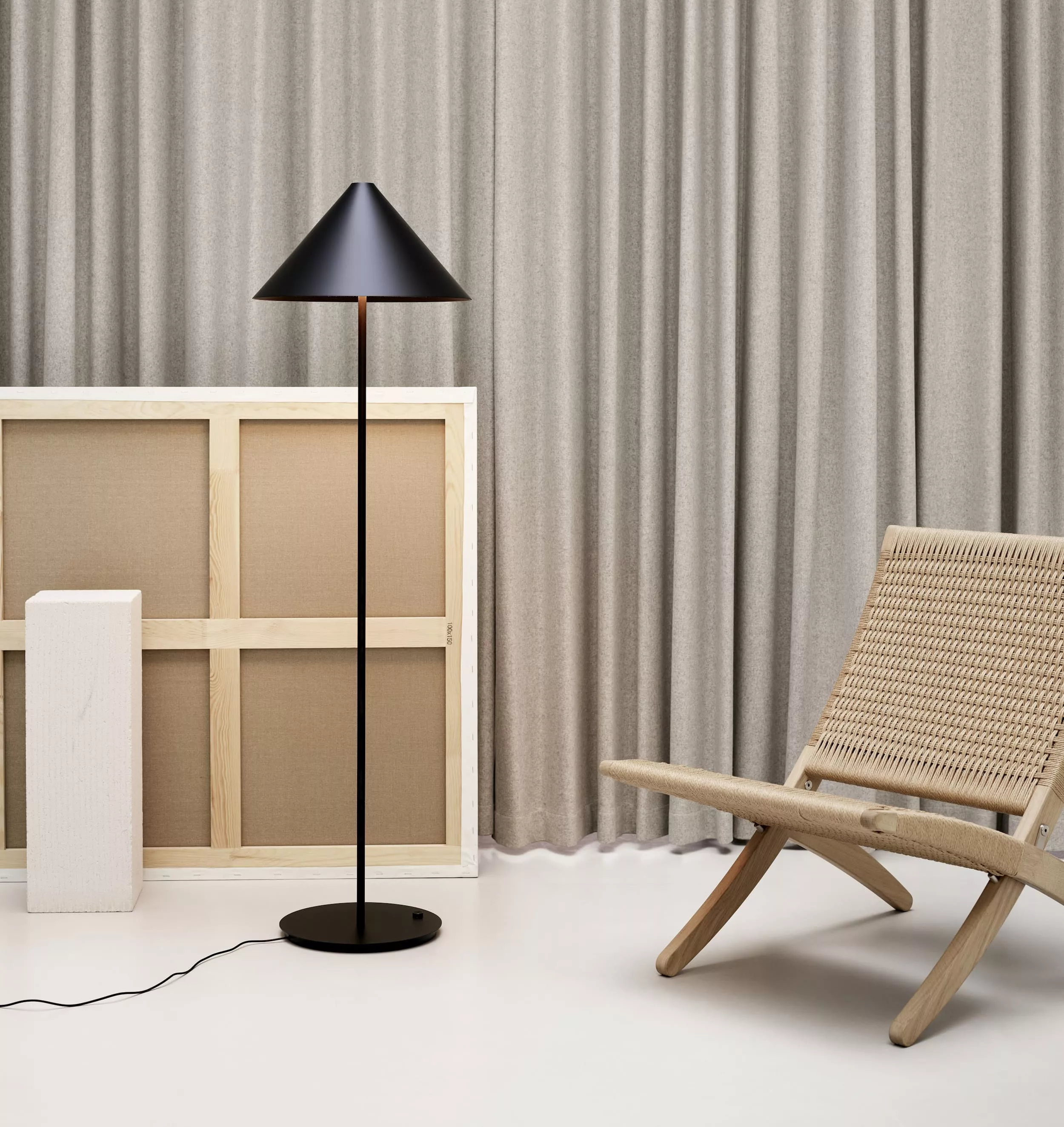 Stehleuchte Louis Poulsen Keglen in Schwarz vor beigem Vorhang, neben Holzstuhl und Leinwand, moderne Inneneinrichtung.