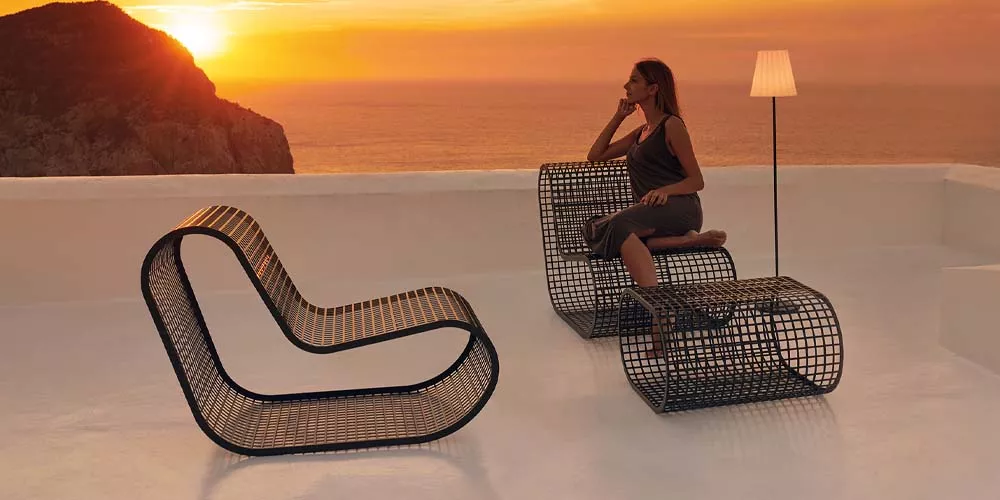 Frau sitzt auf Gandia Blasco Buit Möbeln in Schwarz bei Sonnenuntergang auf einer Terrasse mit Meerblick.