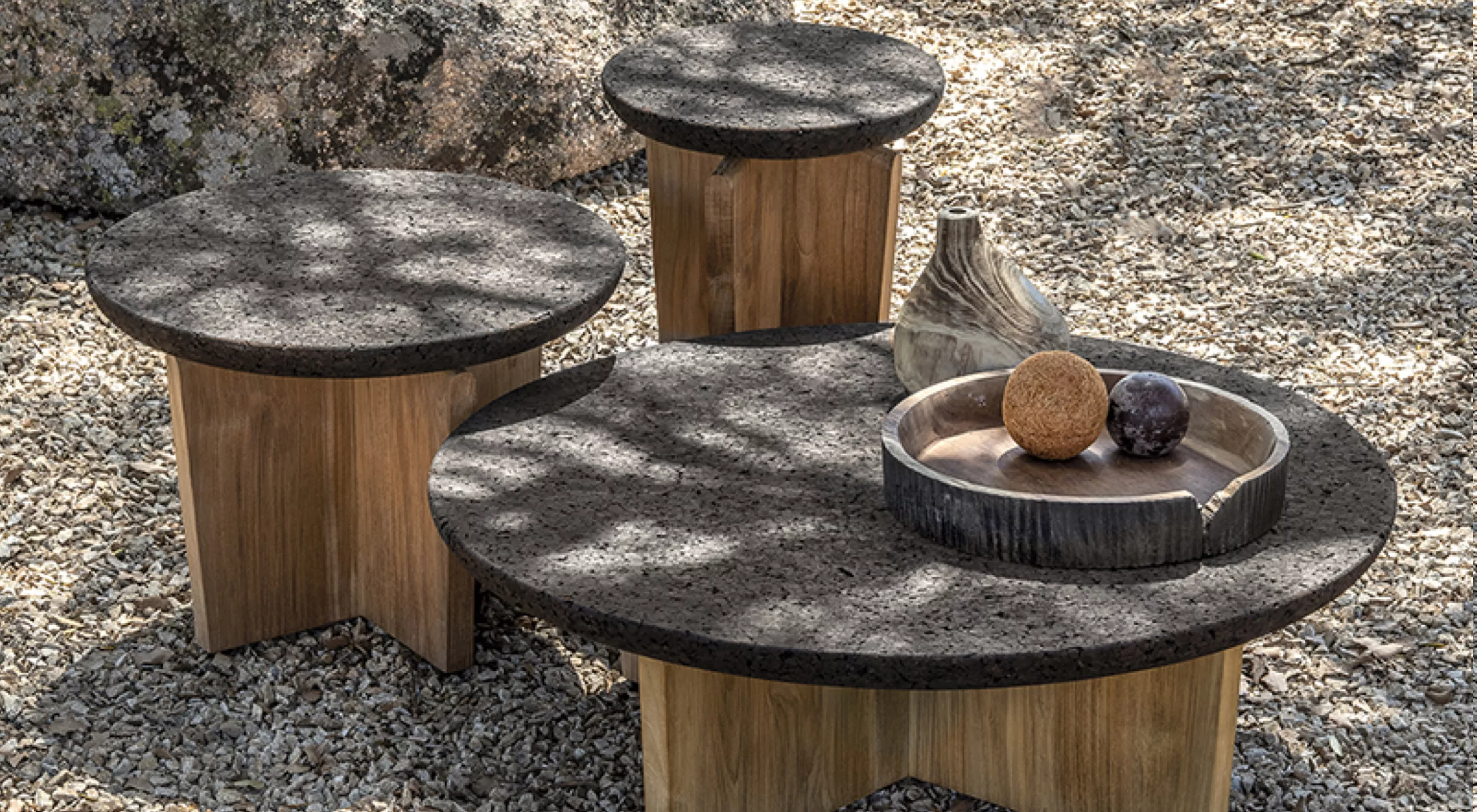 Drei runde Tische von Villa Schmidt aus Holz mit dunklen Steinplatten auf Kiesboden, dekoriert mit einer Vase und Früchten.