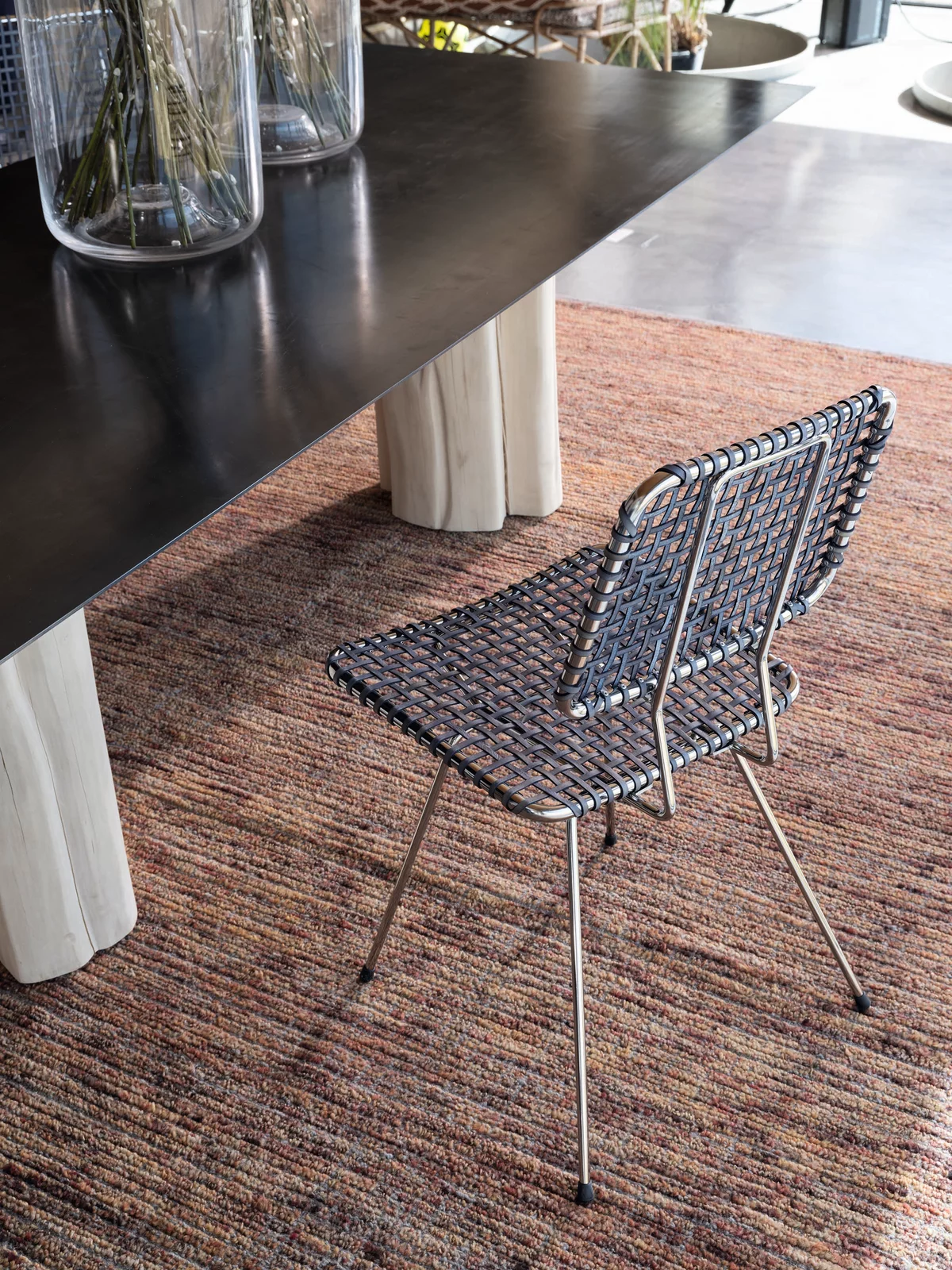 Ein Gervasoni Stuhl aus geflochtenem Material steht auf einem Teppich neben einem Tisch mit Holzbeinen und Glasvasen in einem modernen Raum.