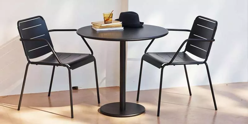 Zwei schwarze Cane-line Go Stühle und ein runder Tisch auf einer Terrasse mit Sonnenlicht und einem Buch auf dem Tisch.