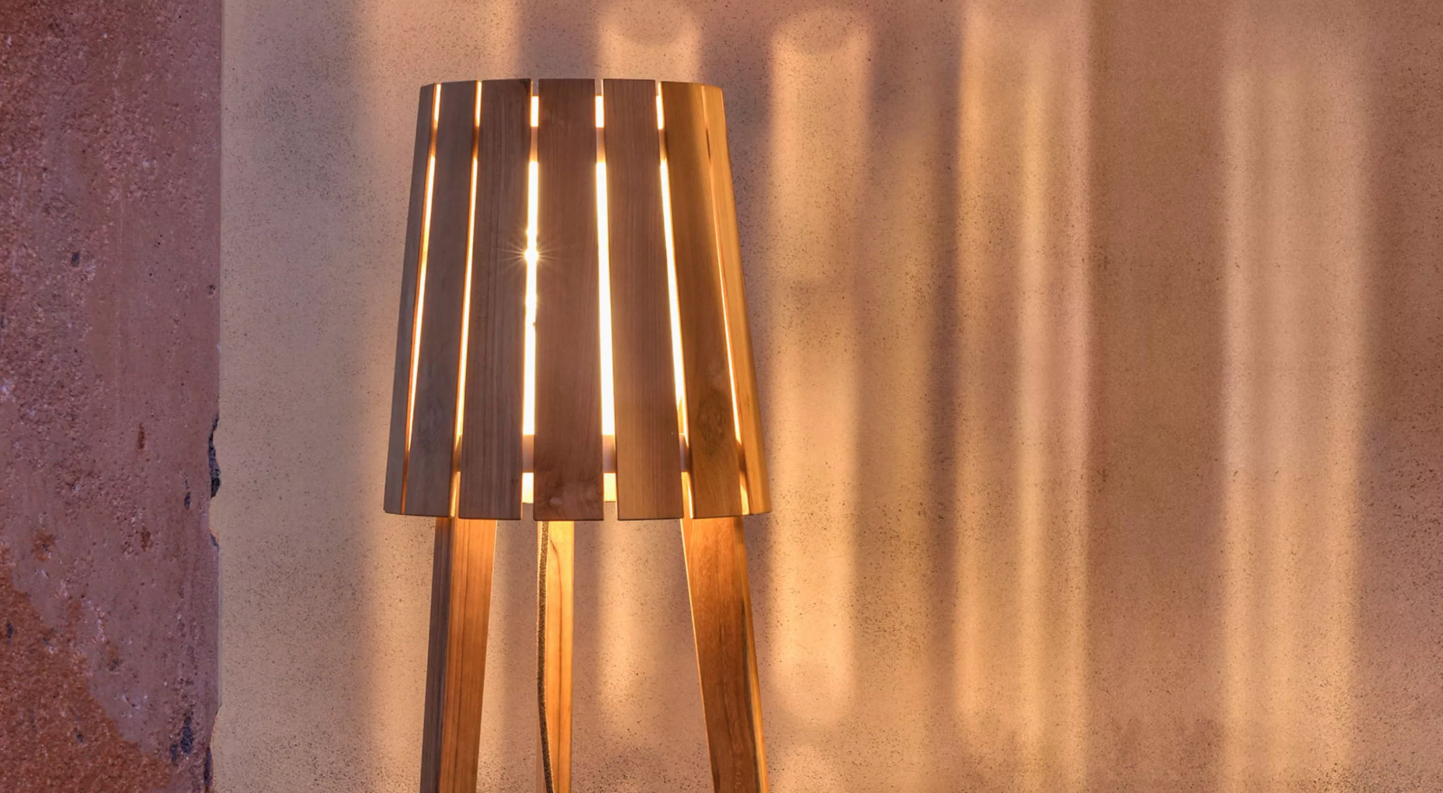 Holzlampenschirm von Villa Schmidt, warmes Licht, stimmungsvolle Beleuchtung vor einer strukturierten Wand.